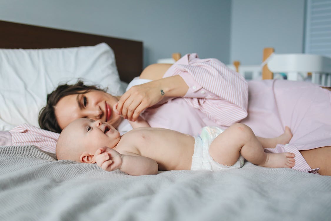 Free Mother Lying Down on Bed Next to Her Baby Stock Photo